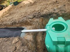 A green septic tank connected to a white pipe and drainage trench filled with gravel.