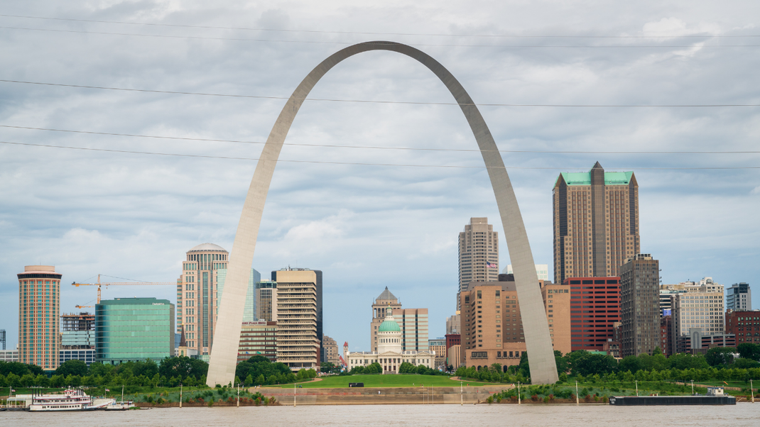 Gateway Arch in St. Louis, Missouri, towering over the city skyline and the Mississippi River, under a cloudy sky.