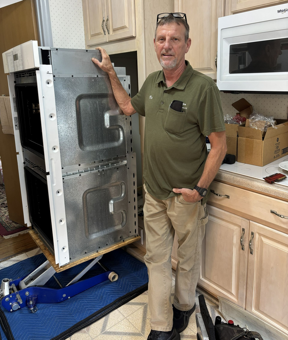 Refrigerator repairman in blue overalls, inspecting the open refrigerator door in a kitchen.