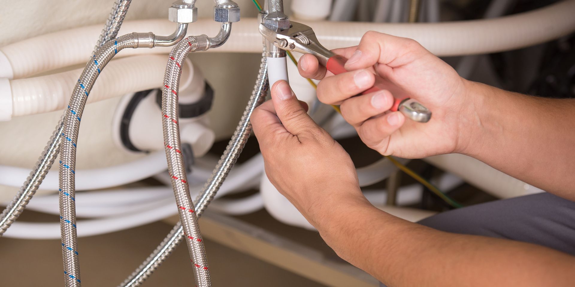 A person is fixing a faucet with a pair of pliers.