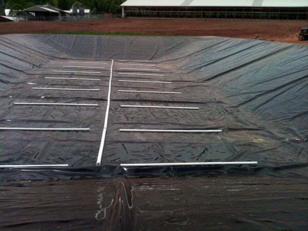 Black liner in a large, empty pond with white pipes running across it. The setting appears to be rural.