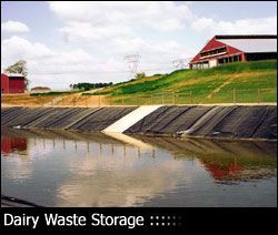 Dairy waste storage pond on a farm with a red barn and green hill in the background. The pond has a dark liner.