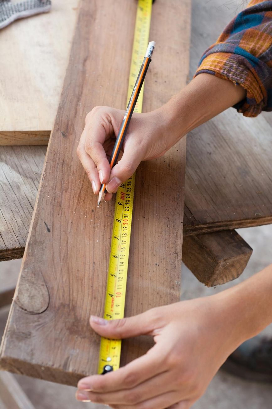 A person is measuring a piece of wood with a tape measure and pencil.