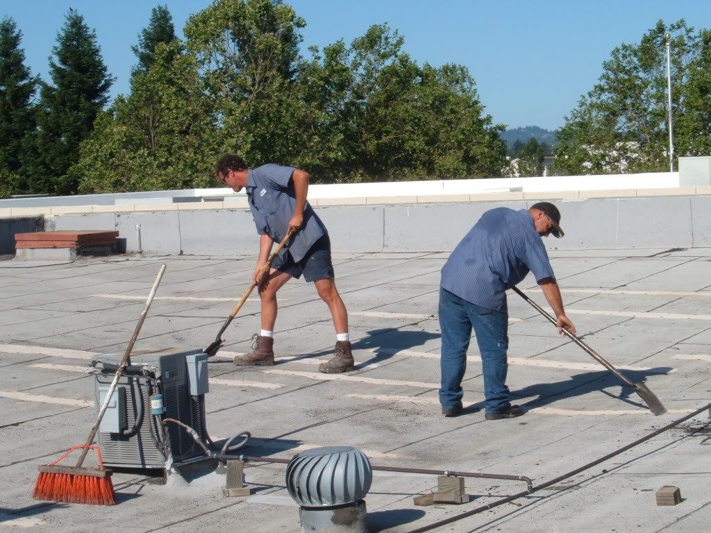 Two men are sweeping a roof with brooms