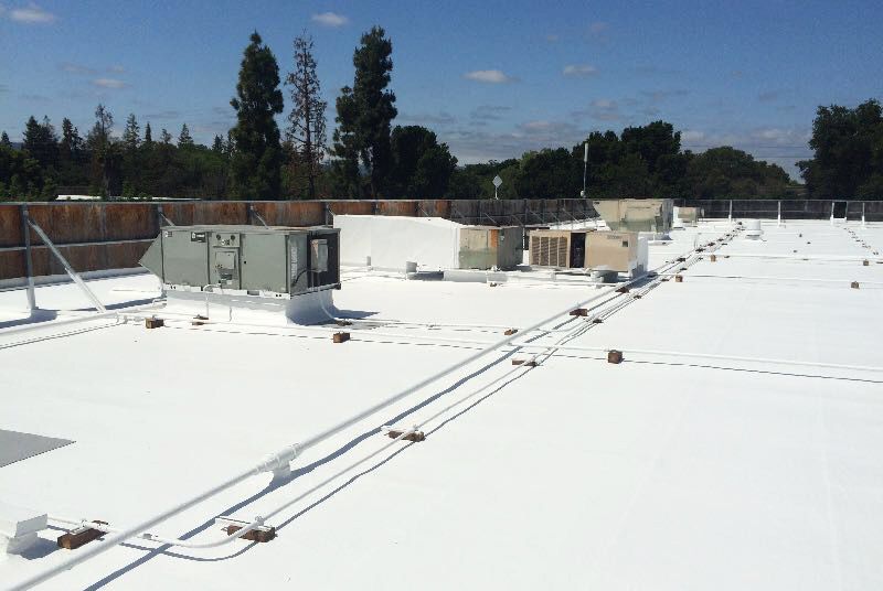 The roof of a building with a white roof and trees in the background.