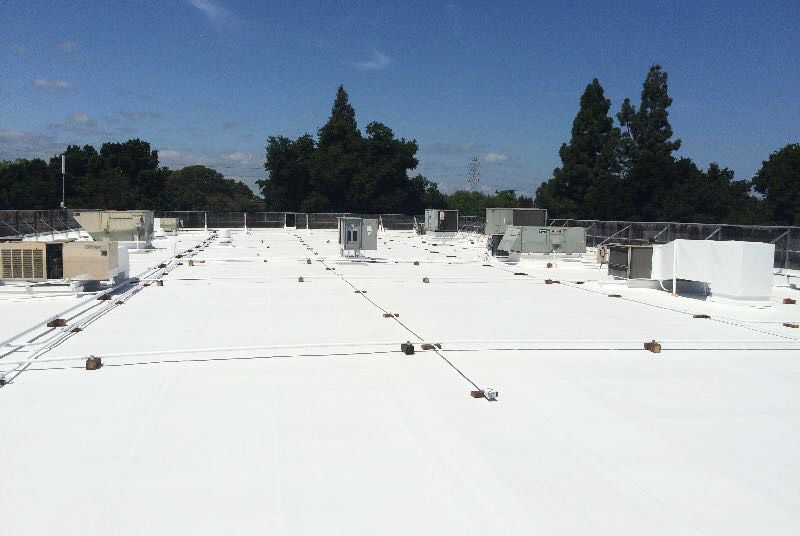 The roof of a building with a white roof and trees in the background.