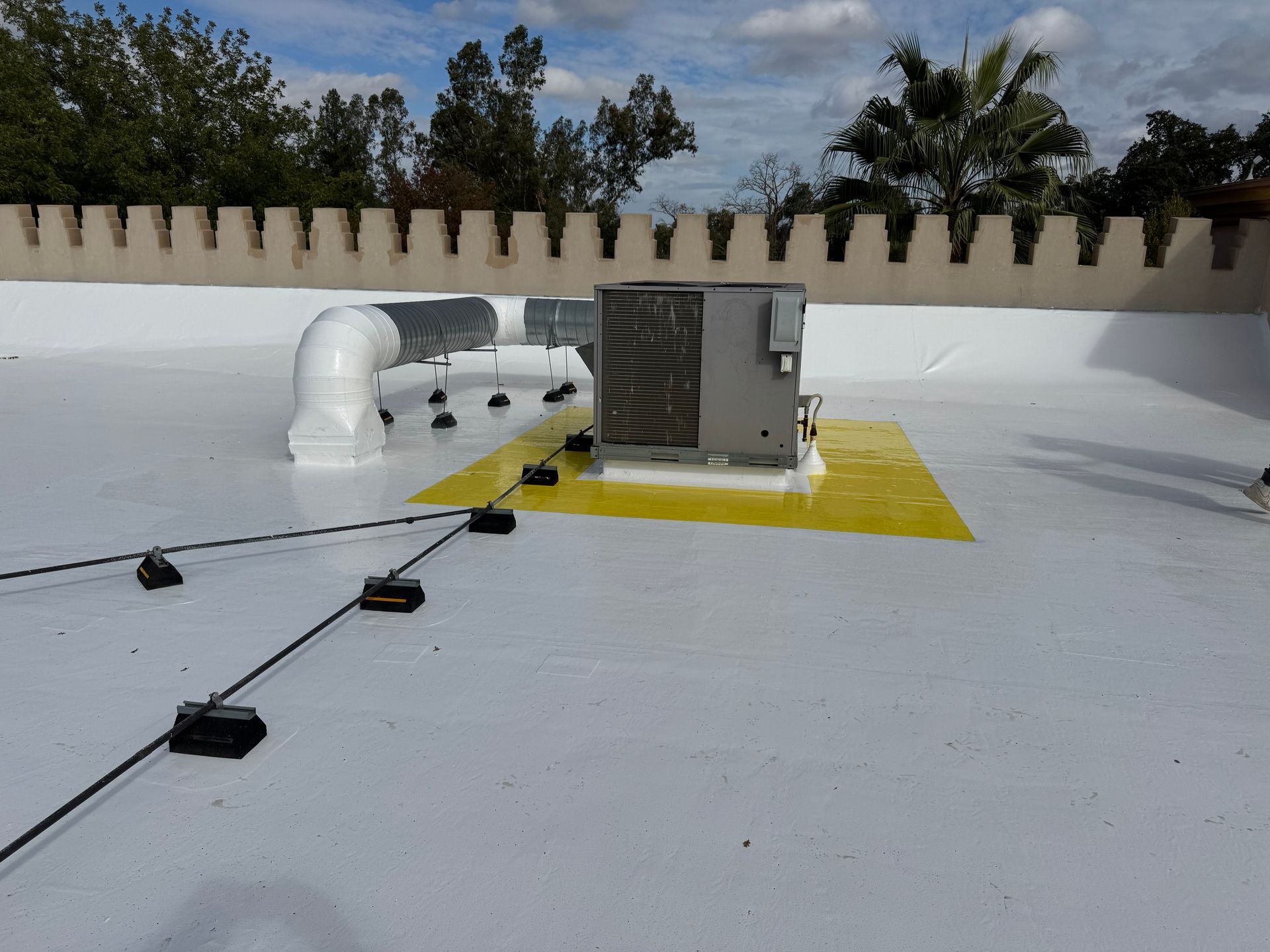 White flat roof with HVAC unit, ductwork, and black cables.