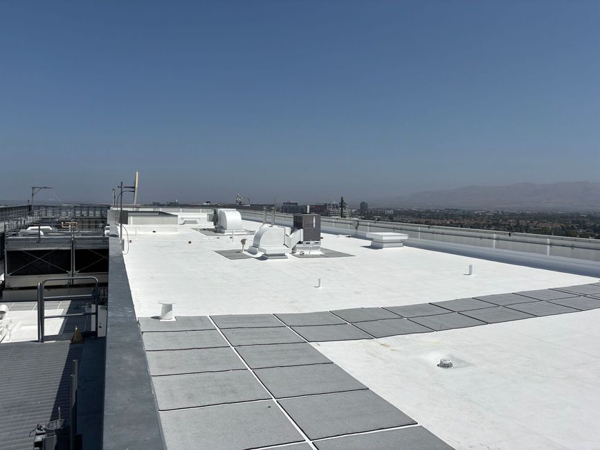Rooftop with white surface and equipment, Blue sky and distant buildings.