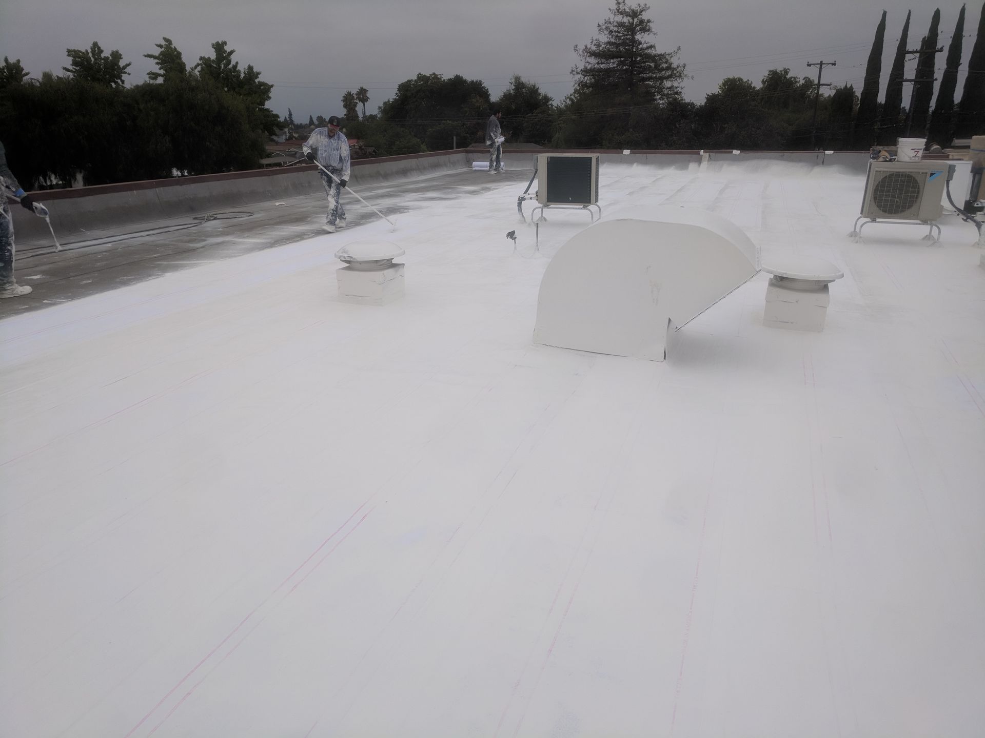 A man is spraying white paint on a roof.