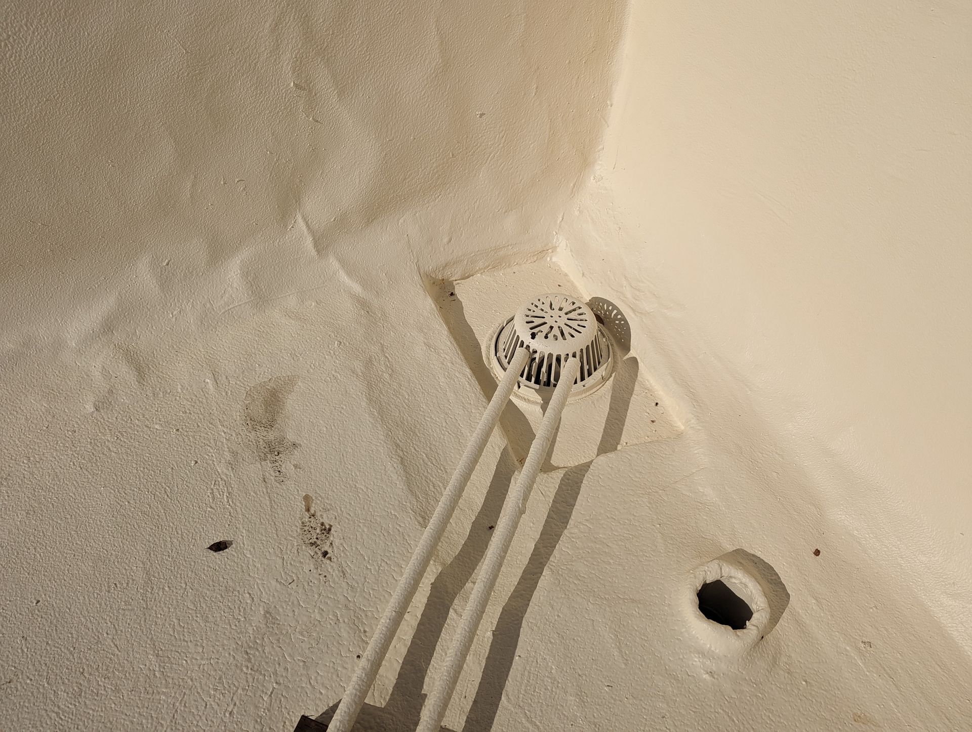 A close up of a drain on a white wall.