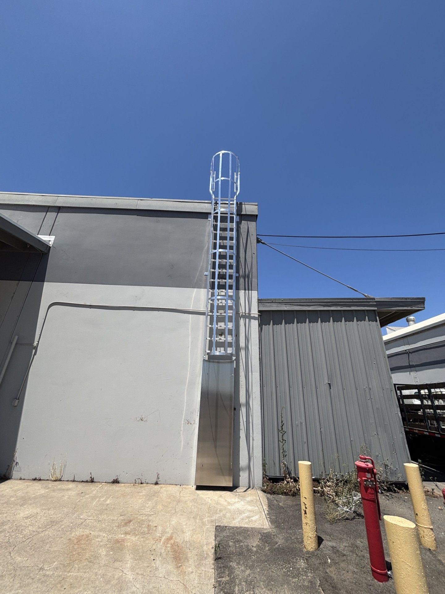 Ladder on exterior building, gray walls, blue sky.