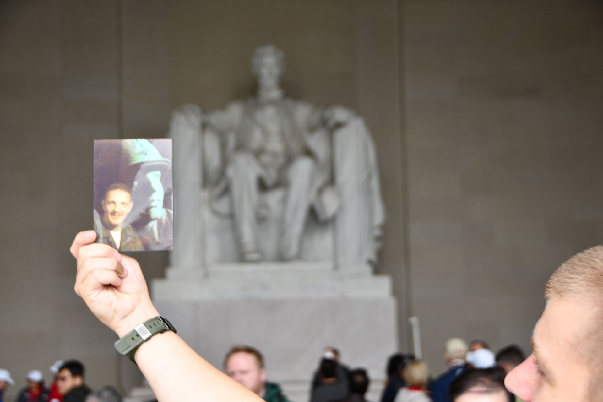 Man holds photo of himself in front of Lincoln Memorial statue.