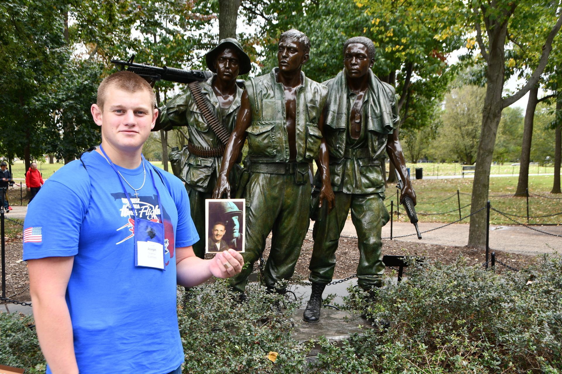 Man at Vietnam Veterans Memorial statue, holding a photo.