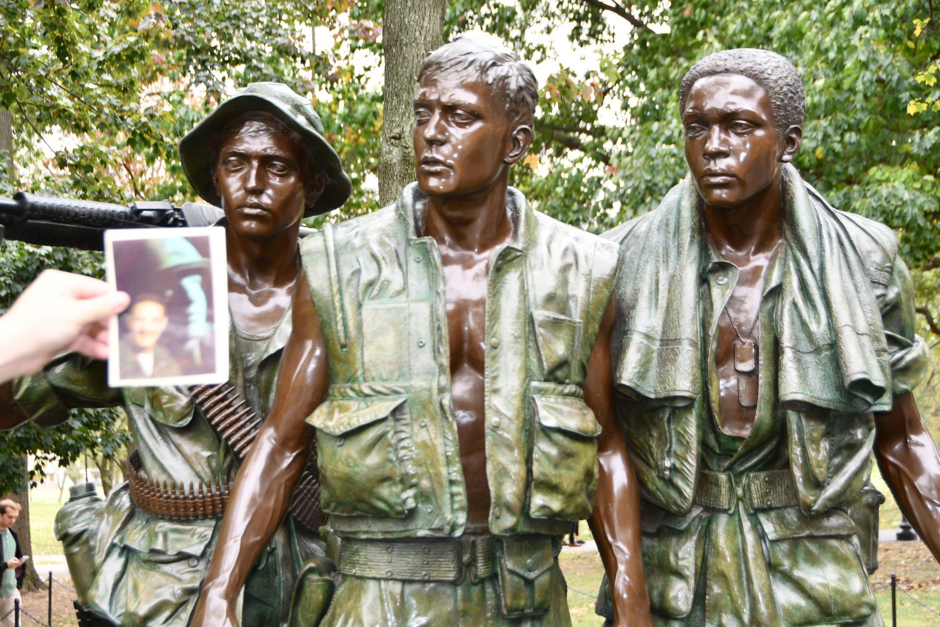 Bronze statue of three soldiers in Vietnam War attire, a photo held up beside it.