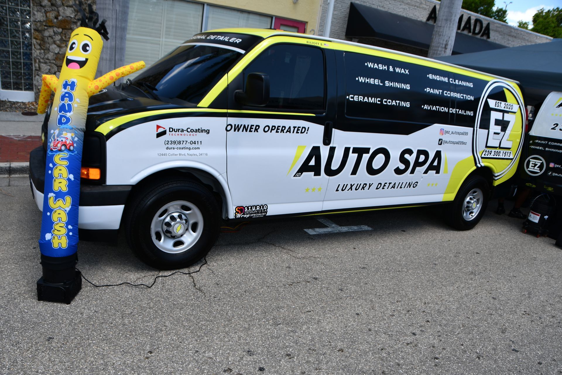 Promotional car wrapped in white, black, and yellow Auto Spa branding beside a blue inflatable mascot stand