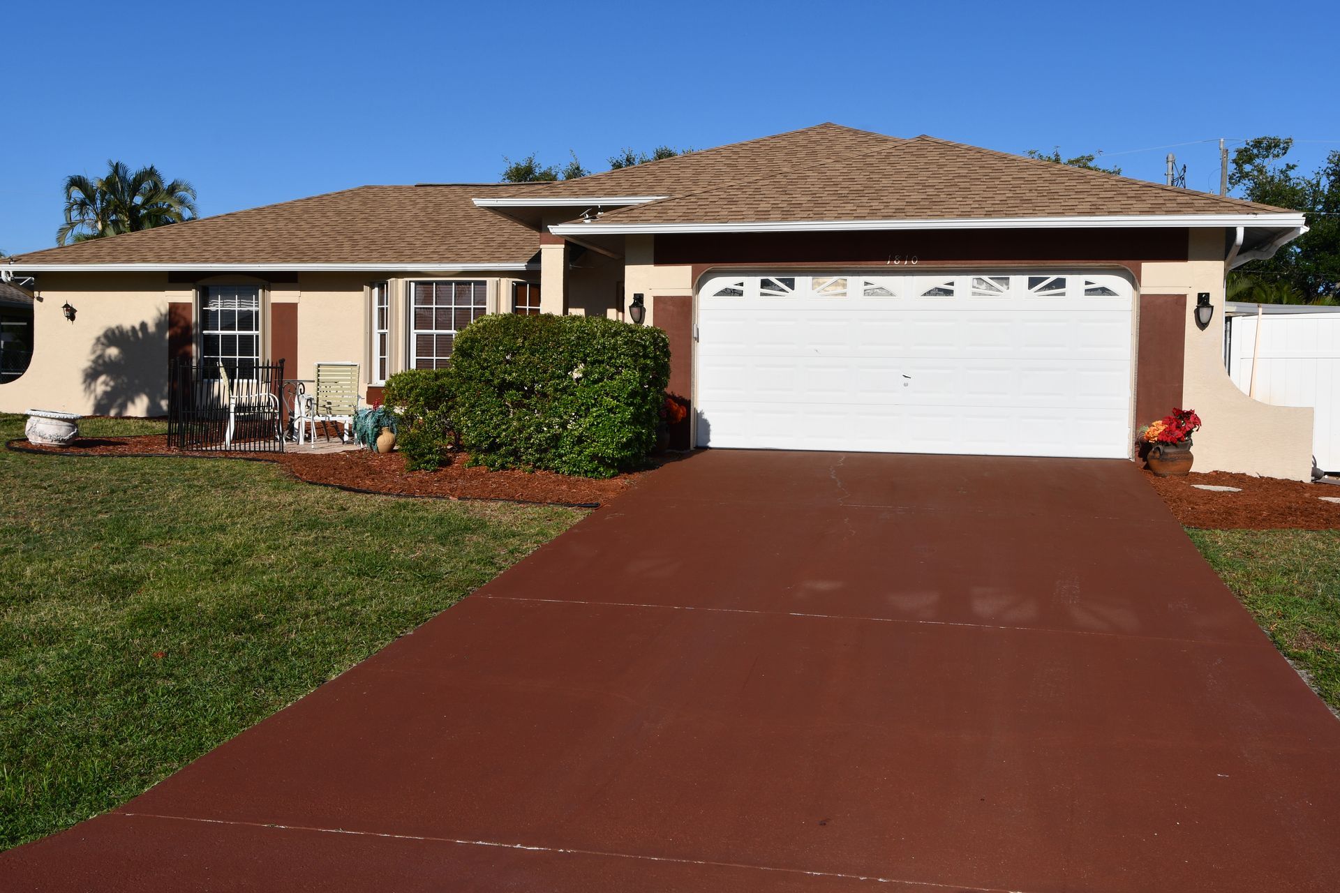 Single-story suburban house with a red driveway and white garage door under a clear sky