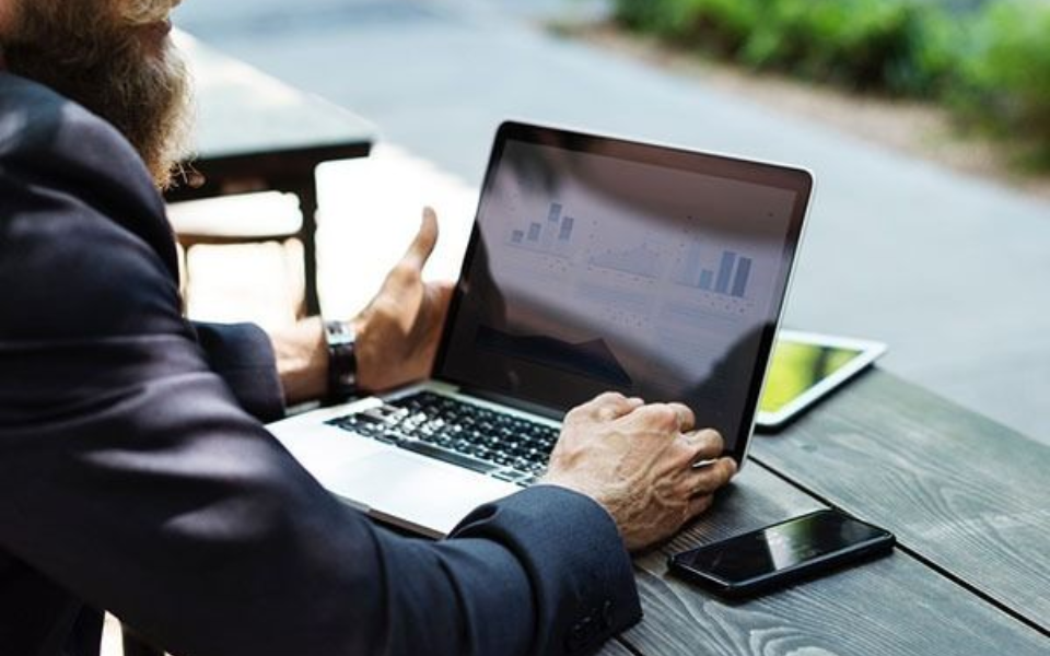 Man in suit working on laptop outdoors, with phone and tablet nearby.