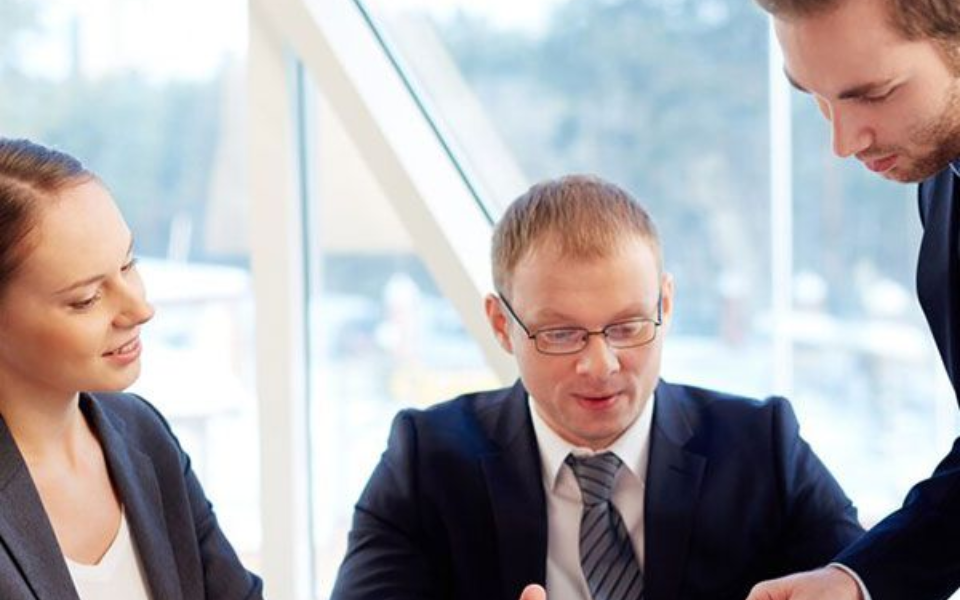 Three business people in suits reviewing documents at a table.