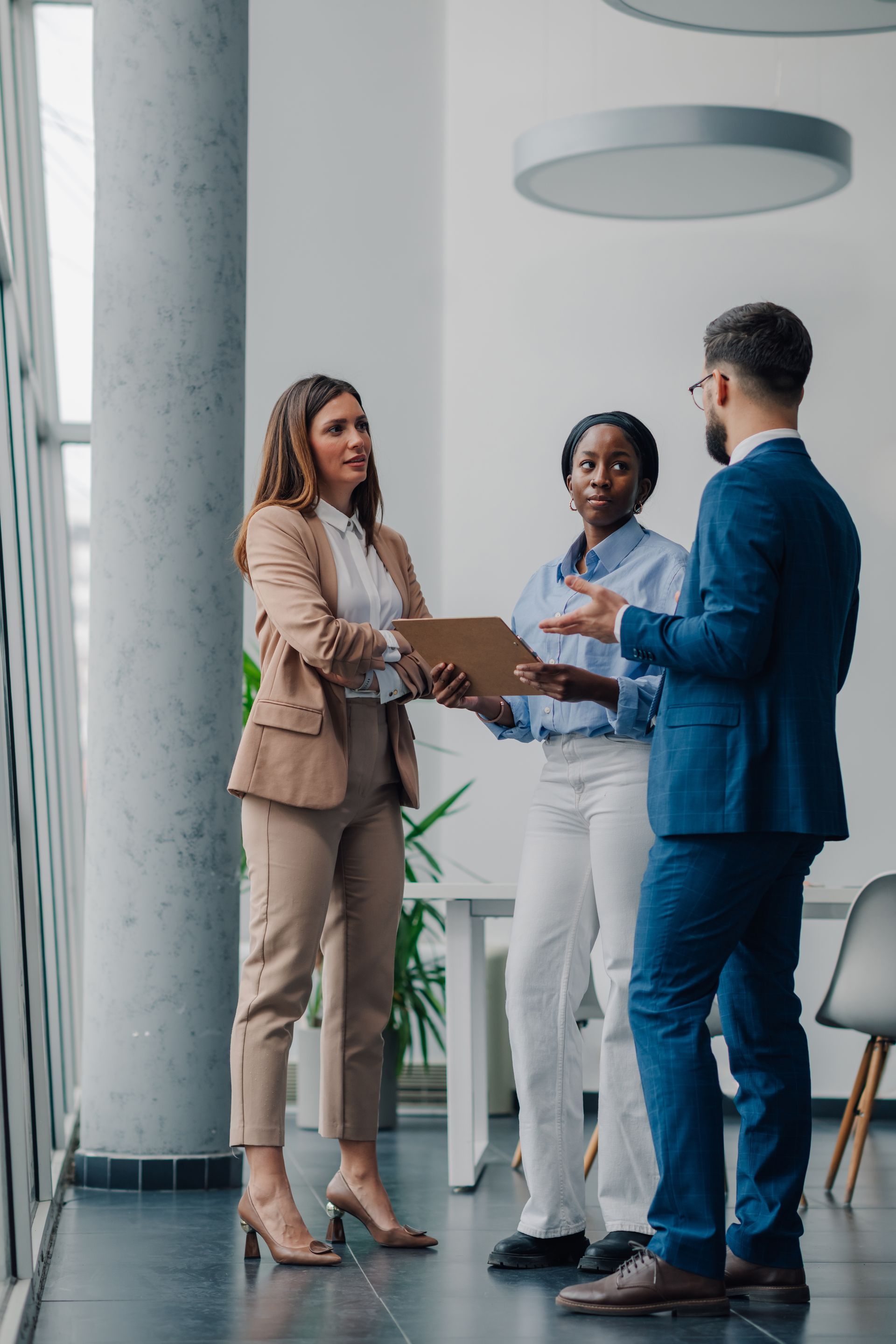 Three people in business attire converse in a bright office setting.