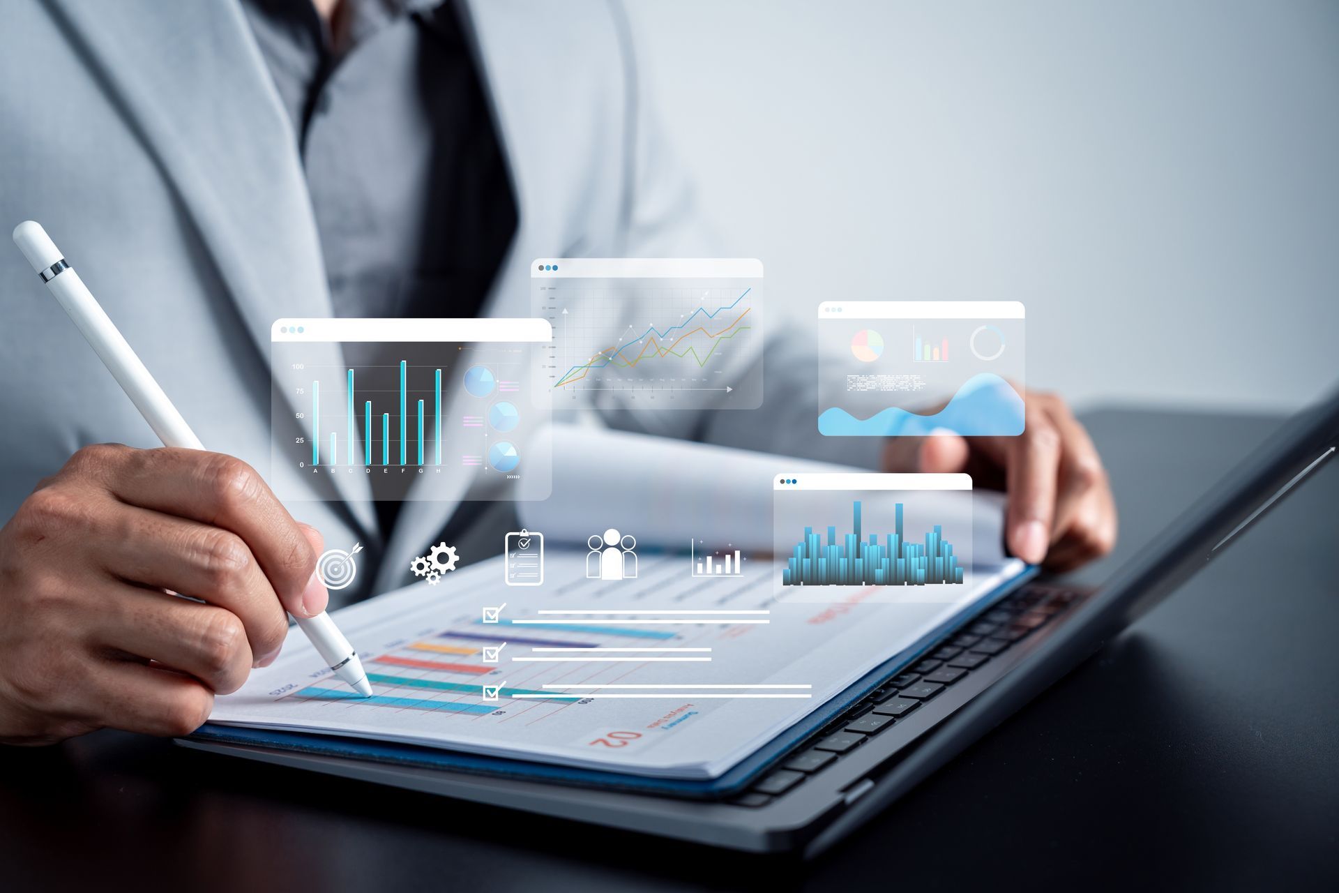 Person in suit reviewing data reports with digital charts overlaid on the paper and a laptop.