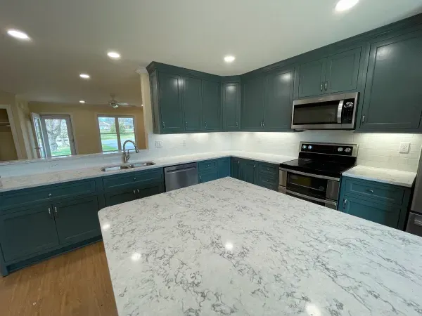 A kitchen with blue cabinets , white counter tops , stainless steel appliances and a large island.