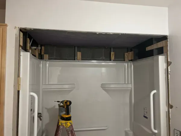 A ladder is sitting in a bathroom next to a shower stall.