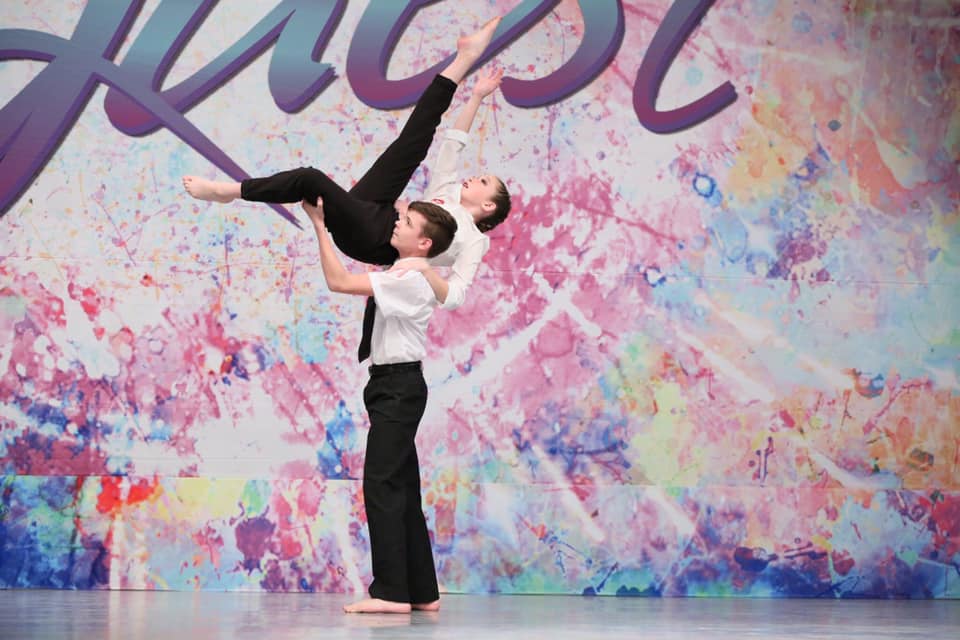 A couple of dancers are dancing on a stage in front of a colorful wall.