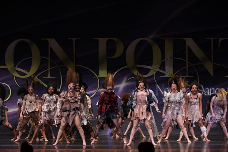 A group of people are dancing in front of a sign that says on point