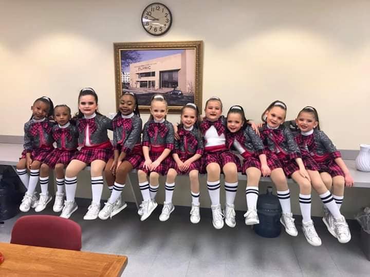 A group of young girls are sitting on a table in front of a clock.