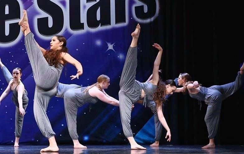 A group of dancers are performing on a stage in front of a sign that says e stars