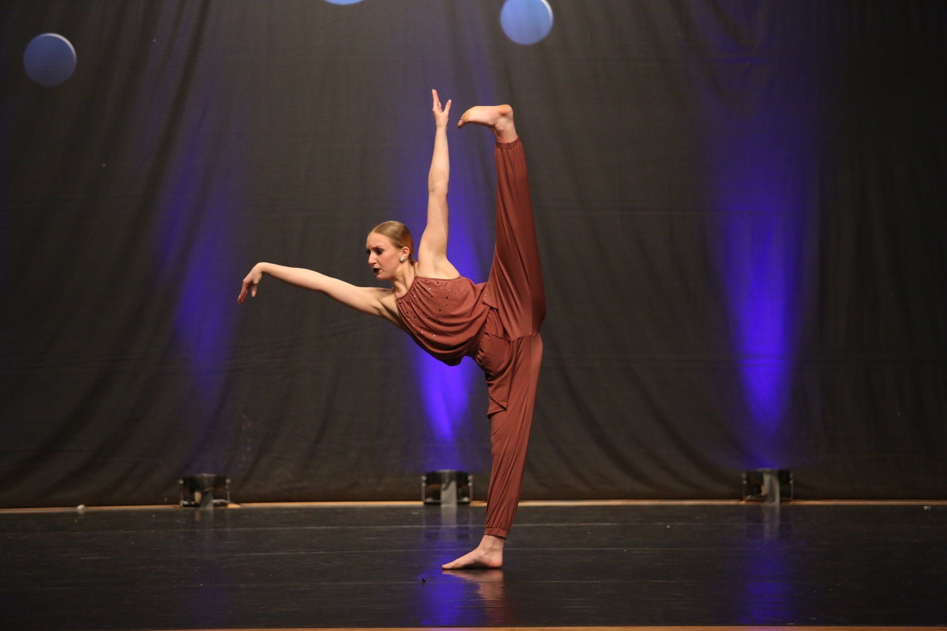 A woman in a red jumpsuit is doing a split on a stage.