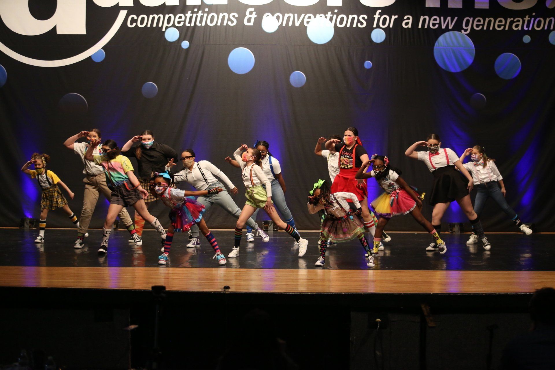 A group of people are dancing on a stage in front of a sign that says competitions & conventions for a new generation