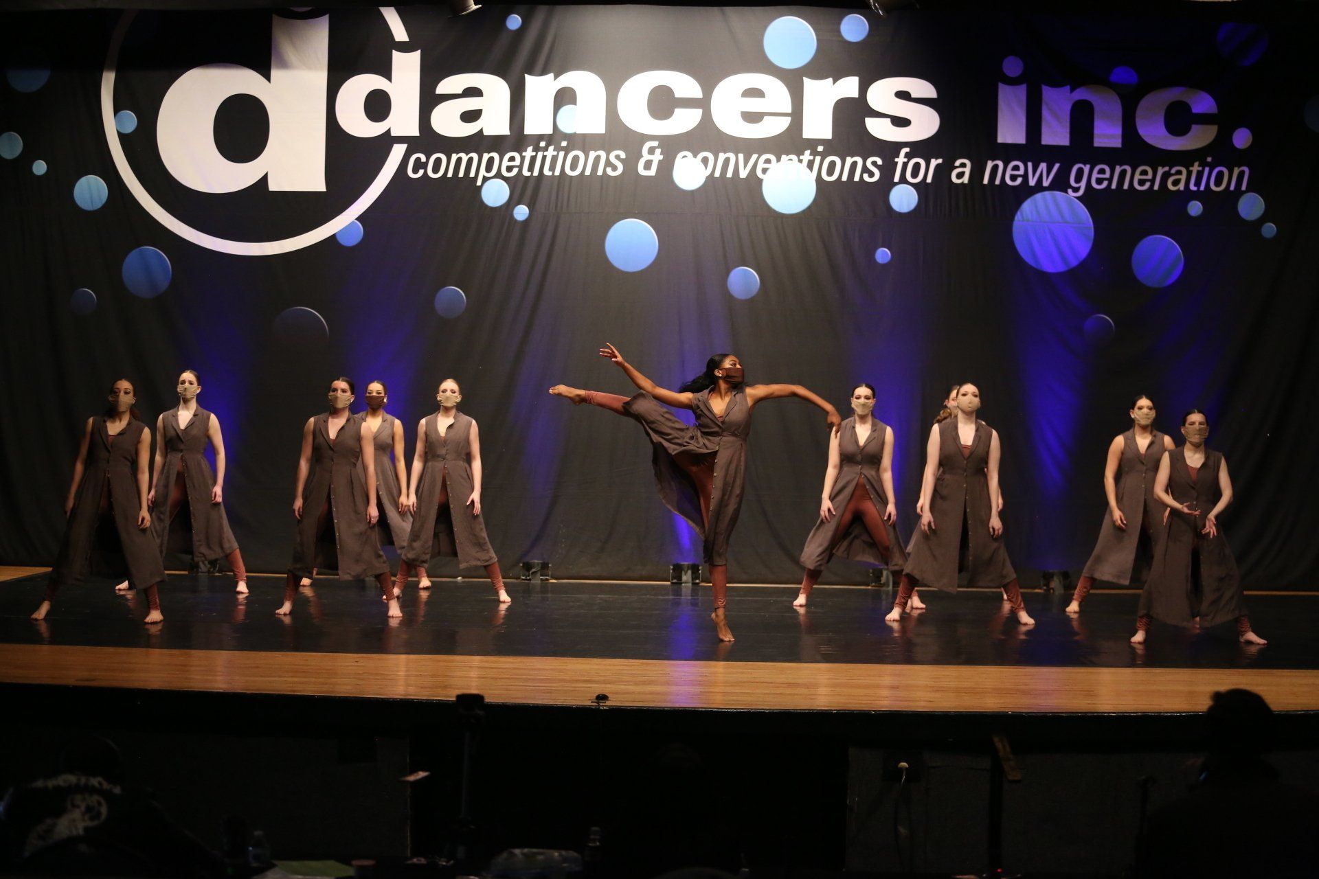 A group of dancers are performing on a stage in front of a sign that says dancers inc.
