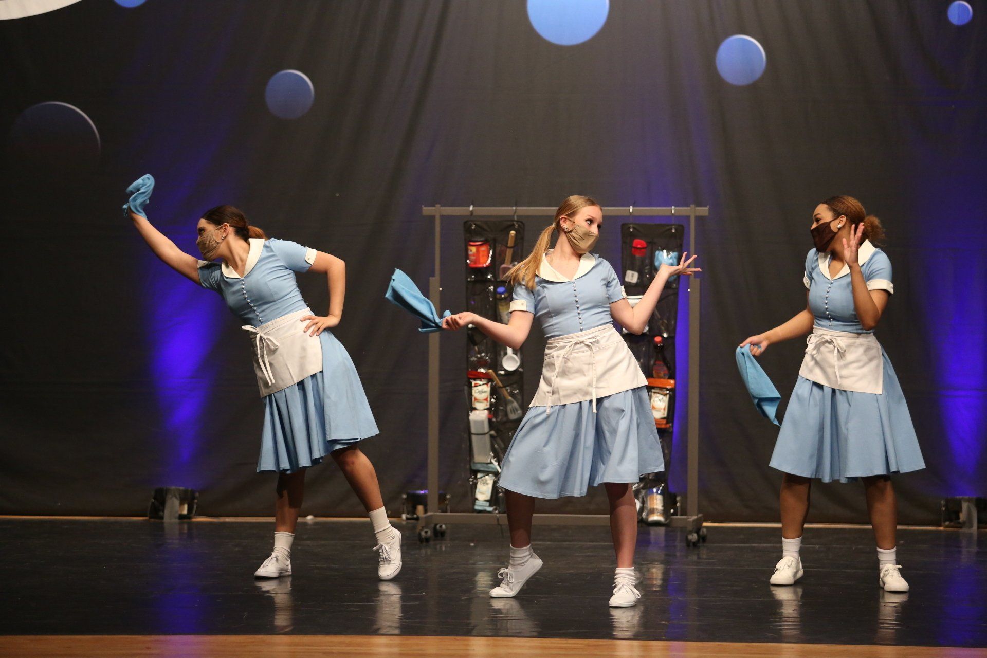 Three women in blue dresses and aprons are dancing on a stage