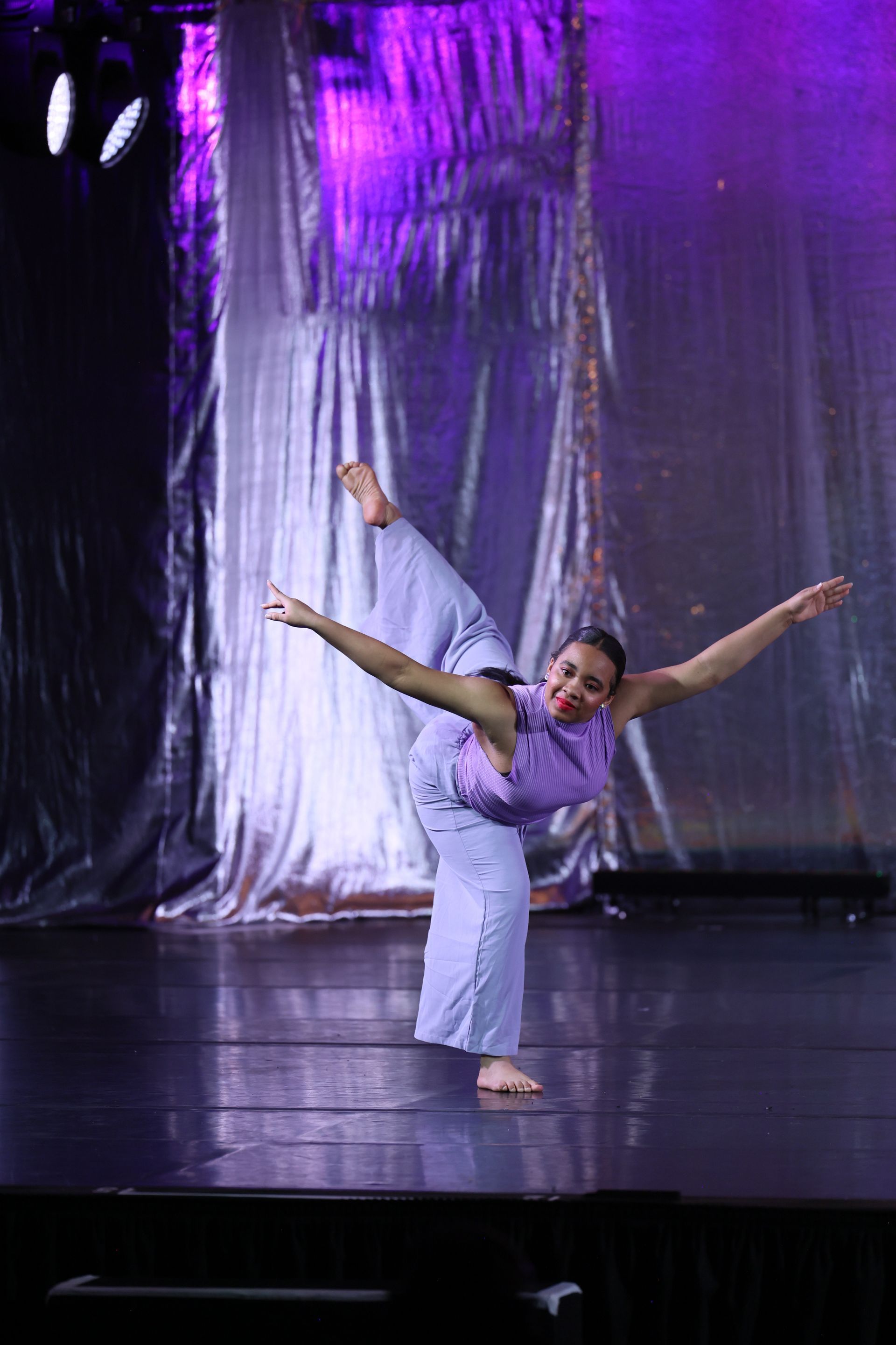 A woman is dancing on a stage in front of a purple curtain.