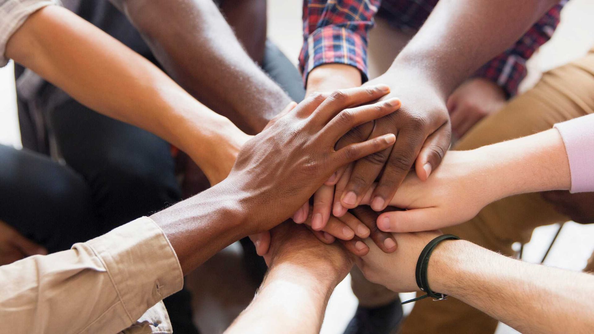 Hands of various skin tones piled together in a gesture of unity.