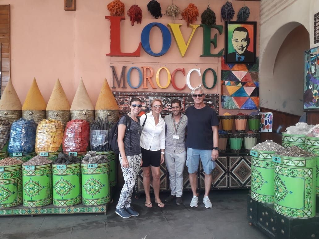 A bustling Moroccan spice souk with colorful piles of spices, herbs, and dried goods displayed in vibrant stalls under arched market passageways.
