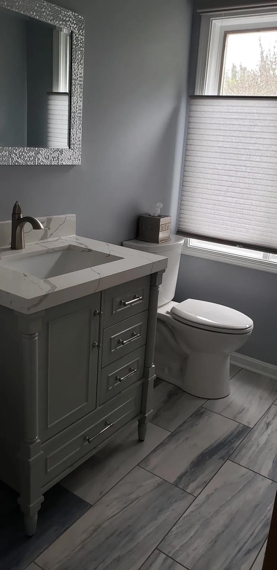 A bathroom with a sink , toilet , mirror and window.