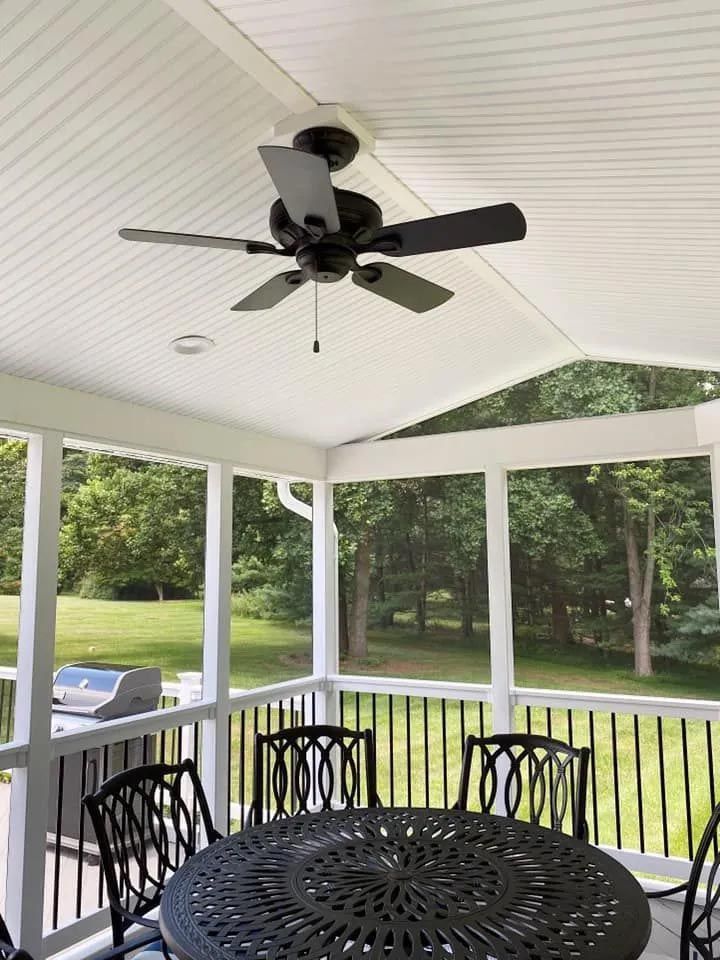 A screened in porch with a table and chairs and a ceiling fan.