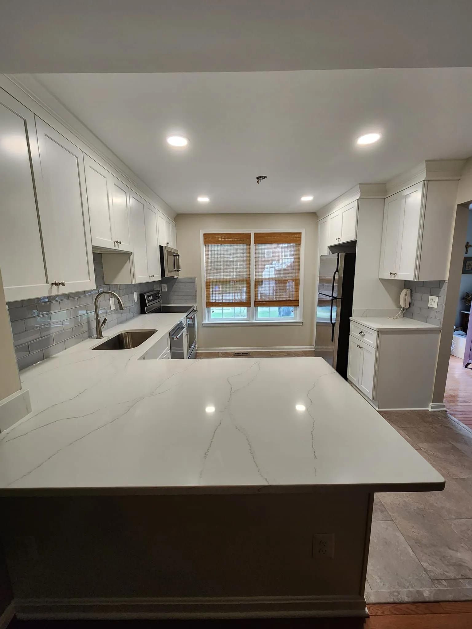 A kitchen with white cabinets , granite counter tops , stainless steel appliances and a large island.