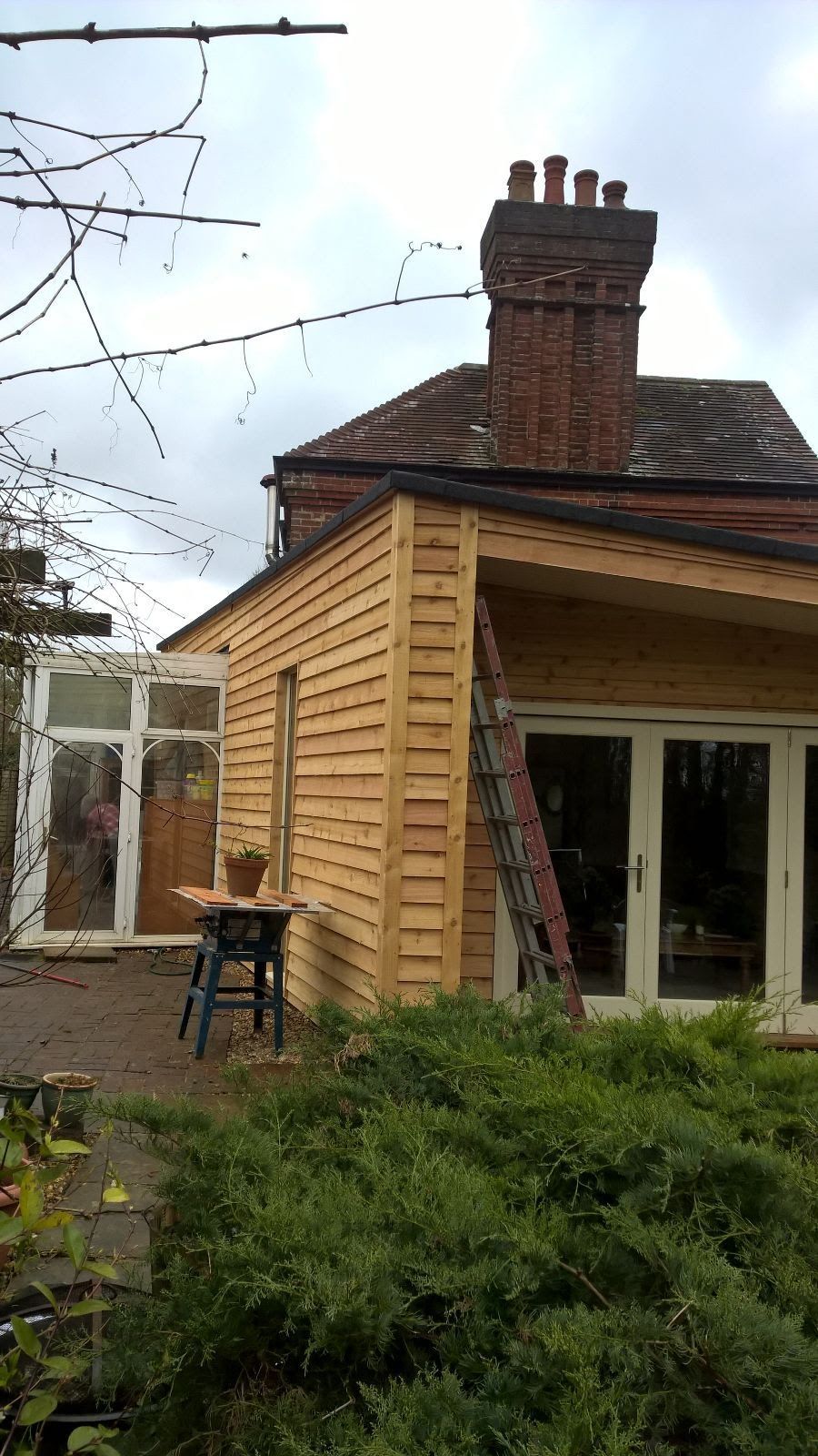 A house with a wooden extension and a ladder in front of it.