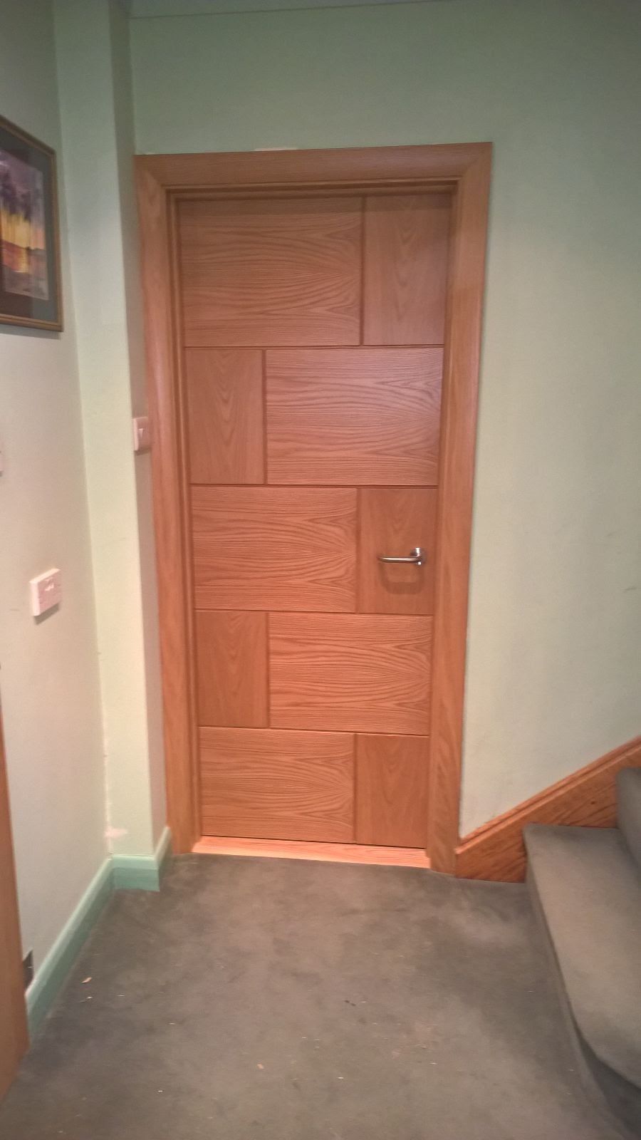 A wooden door is in a hallway next to stairs.