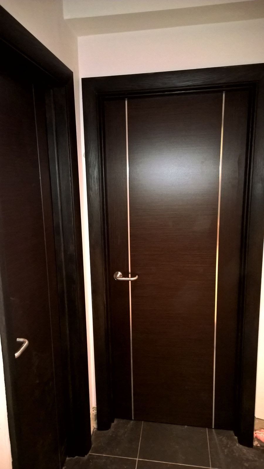 A wooden door with a metal trim is in a hallway.
