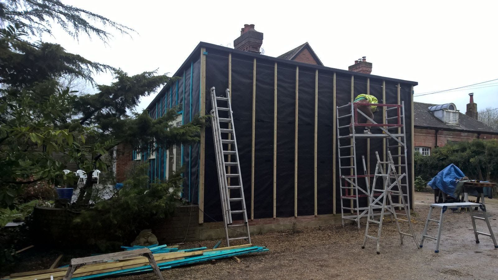 A man is standing on a ladder in front of a building under construction.