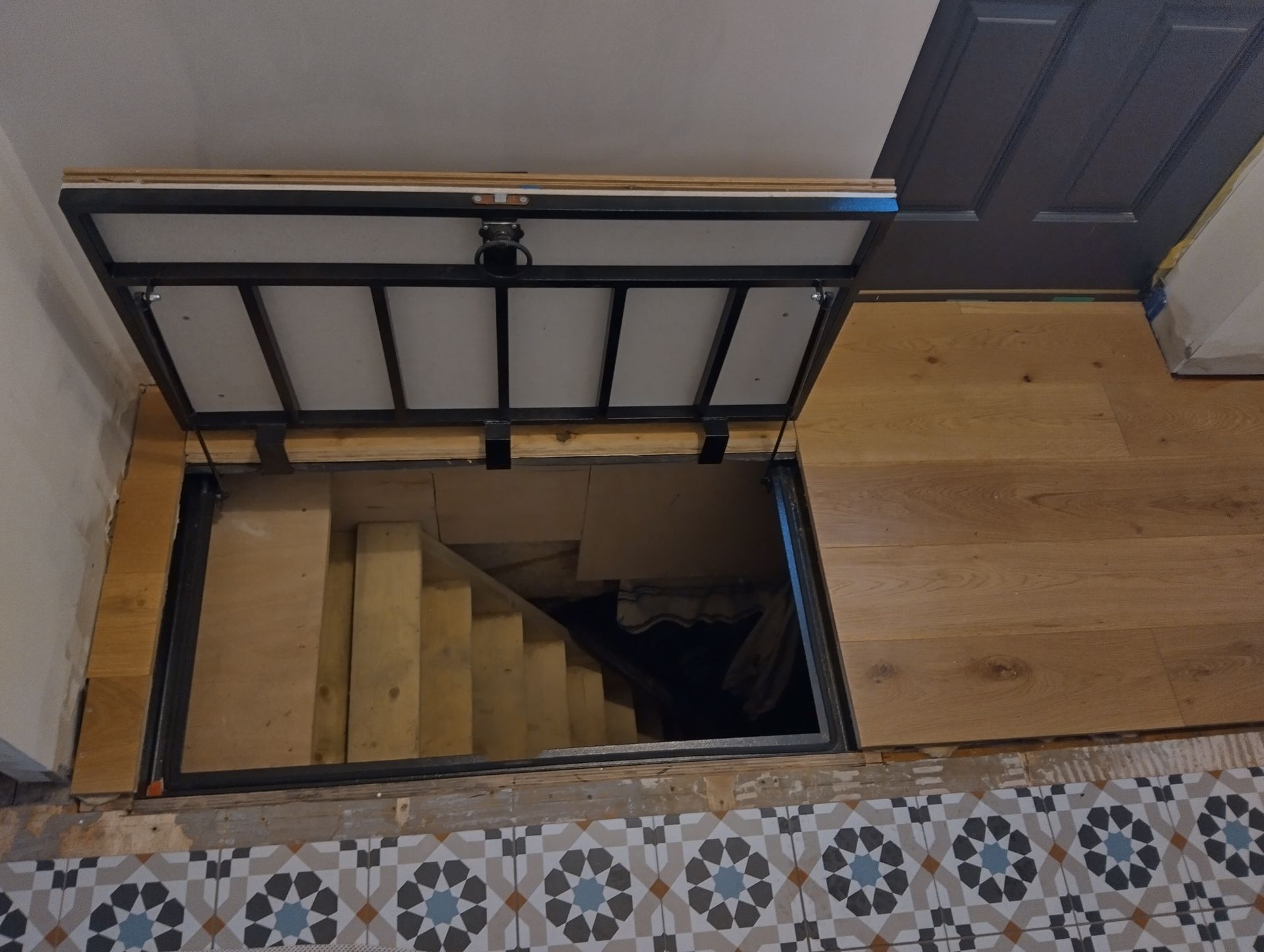 A staircase in a basement with a door open and a wooden floor.