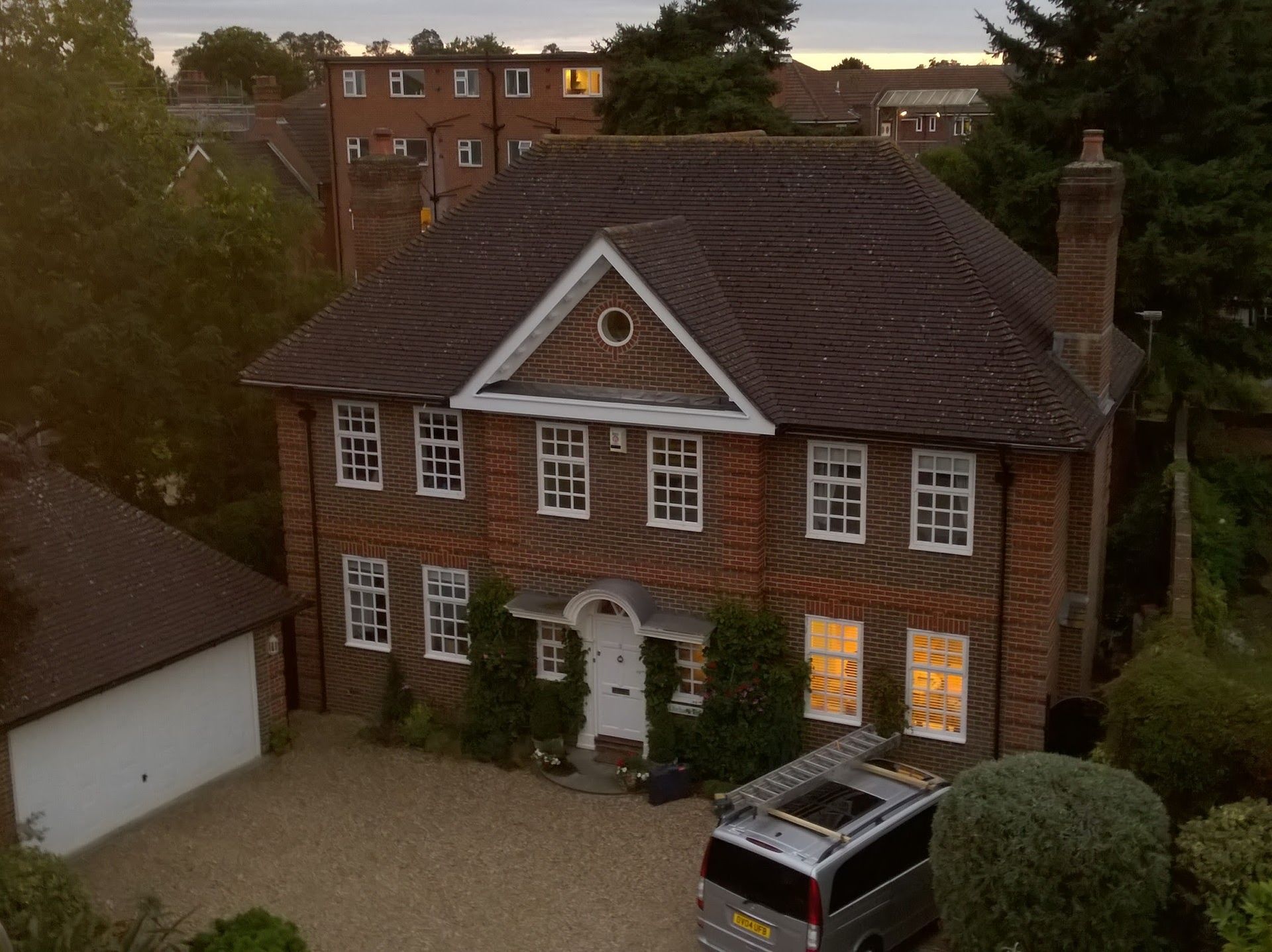 An aerial view of a large brick house with a van parked in front of it