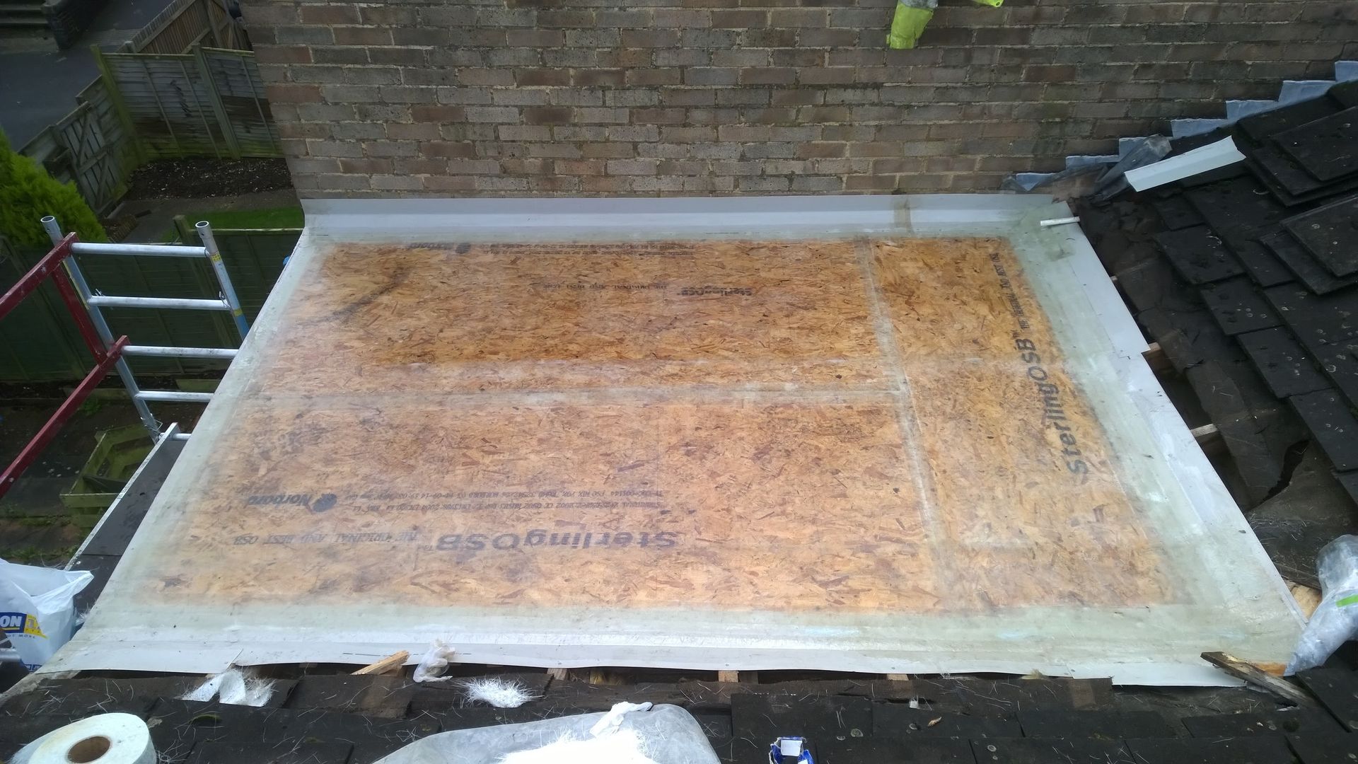 A piece of plywood is sitting on top of a roof next to a brick wall.