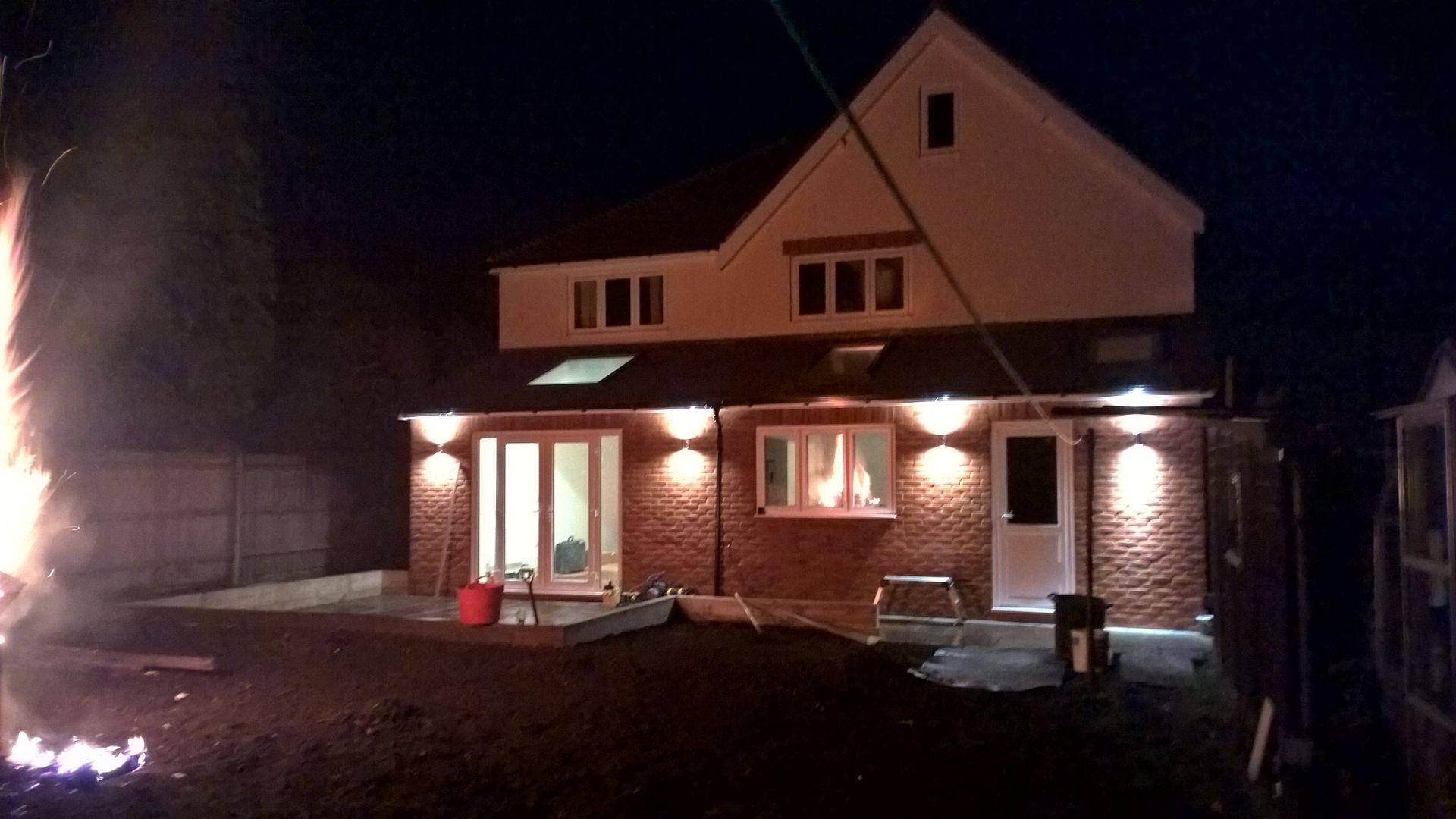 A house is lit up at night with a fire in the background