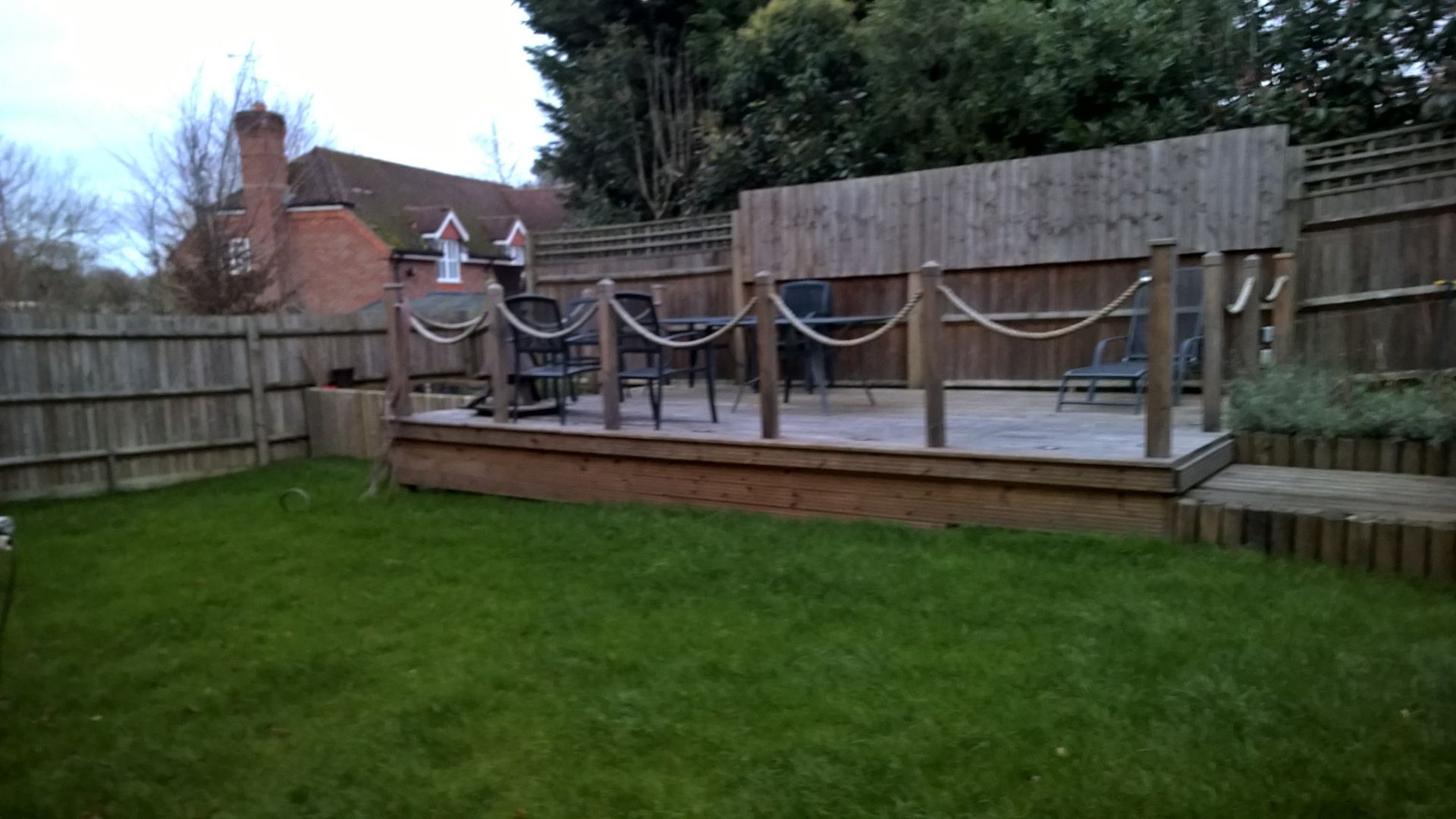 A wooden deck with chairs and umbrellas in a backyard.
