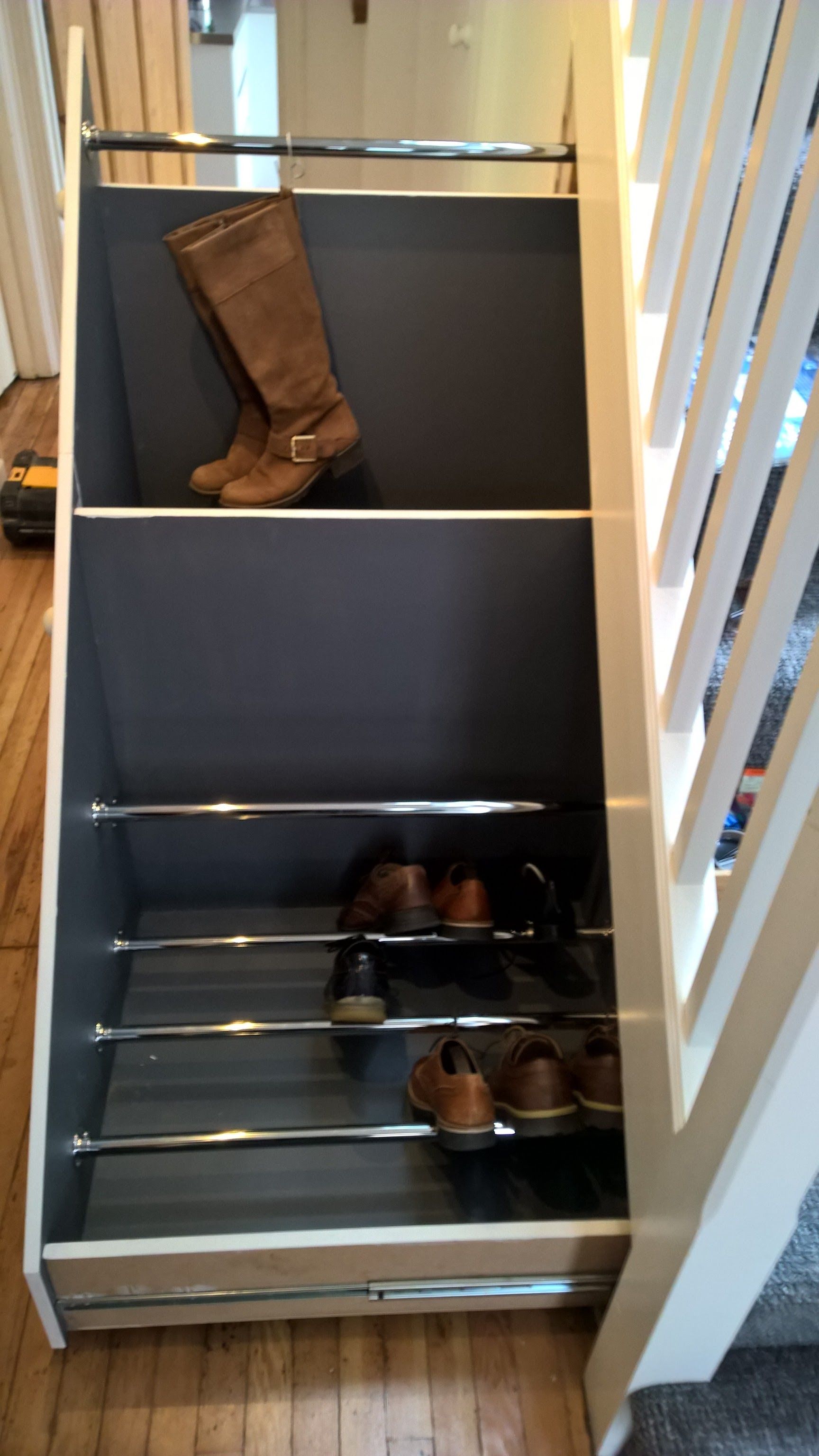 A pair of boots is sitting on top of a shoe rack under a set of stairs.
